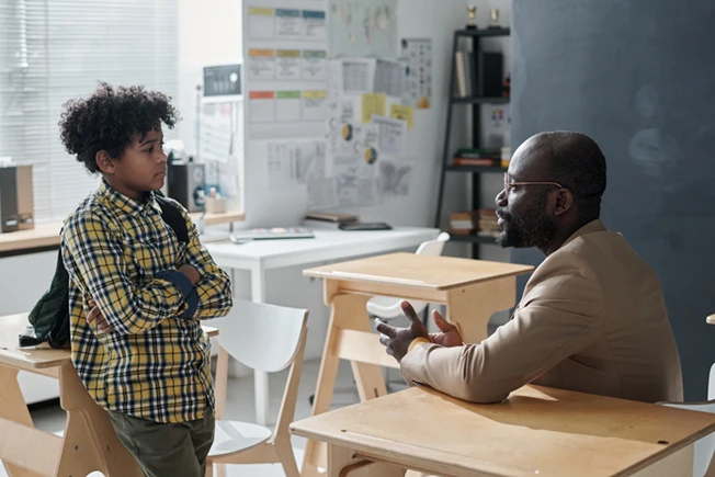 An elementary school student and teacher having a discussion in a classroom after class.