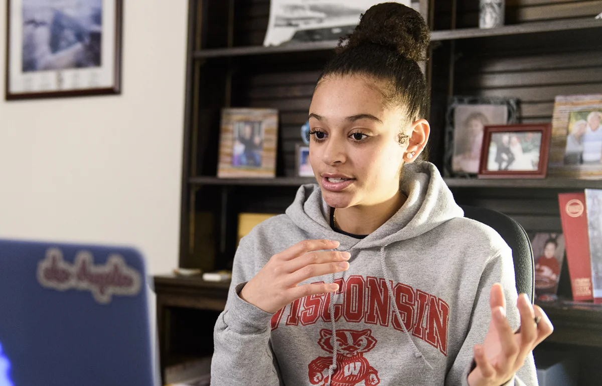 A college student talking and gesturing while looking at a laptop.